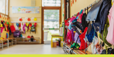colorful backpacks and coats hang from hangers outside a classroom