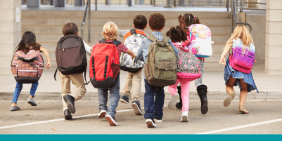 eight young children walking away from the camera, all wearing backpacks