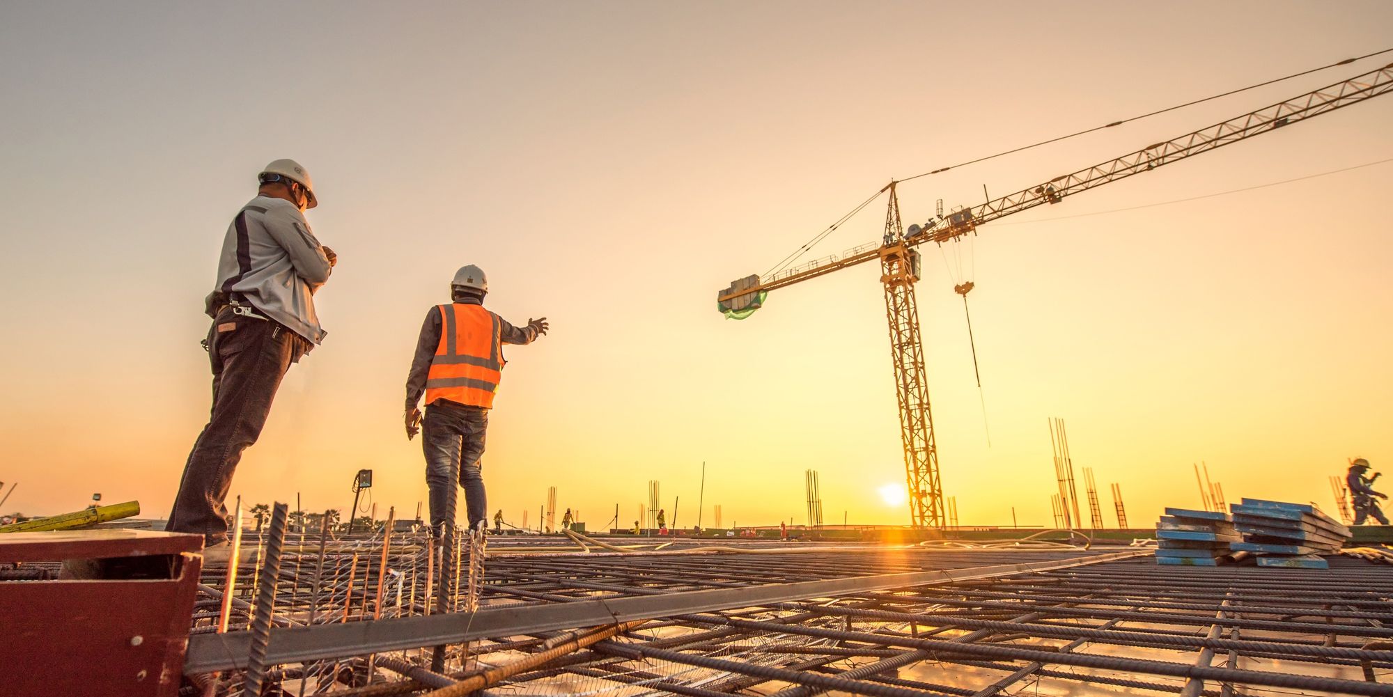 two male construction workers on a job site with the sun in the distance