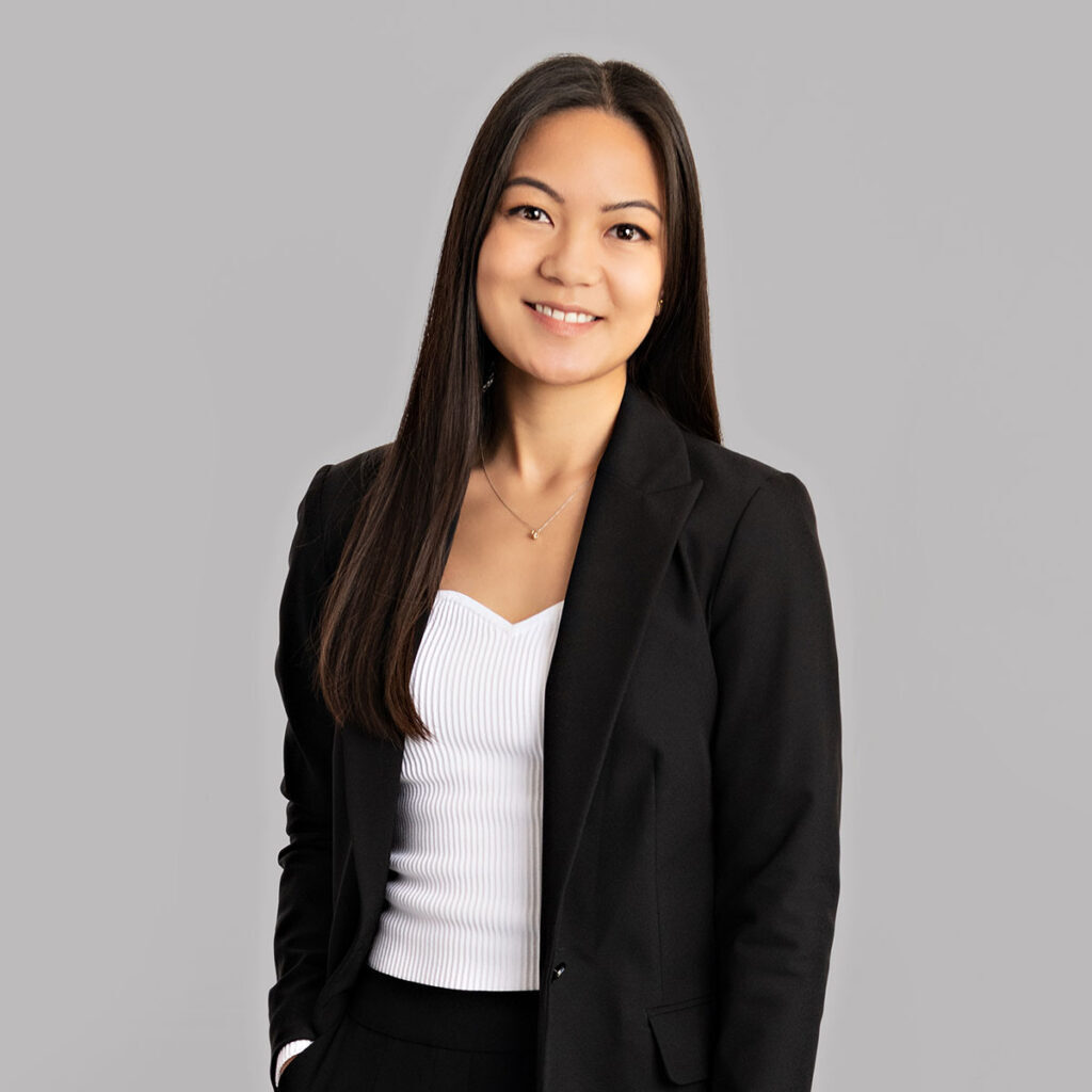Erika A person with long black hair smiles at the camera. They are wearing a black blazer with a white blouse underneath.